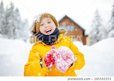 Happy preteen boy having fun playing with fresh snow during snowfall in european Alps. Child dressed in warm clothes, hat, hand gloves and scarf. Happy preteen boy having fun playing with fresh snow during snowfall in european Alps. Child dressed in warm clothes, hat, hand gloves and scarf. 105543355