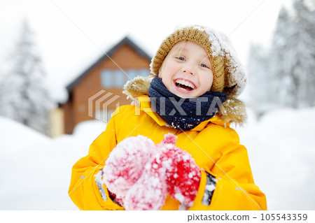Happy preteen boy having fun playing with fresh snow during vacation in european Alps. Child dressed in warm clothes, hat, hand gloves and scarf. 105543359