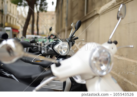 Motorcycle, scooters are parked on the narrow street. In old European cities there is a problem of parking vehicles. Compact transport 105543526