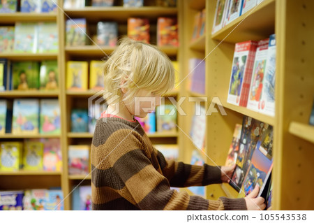 A preteen boy leafing through a book while standing at a bookshelf in a school library or bookstore. A preteen boy leafing through a book while standing at a bookshelf in a school library or bookstore. 105543538
