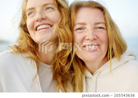 Redhead senior mother and her beautiful adult daughter are walking together and laughing Redhead senior mother and her beautiful adult daughter are walking together and laughing 105543636