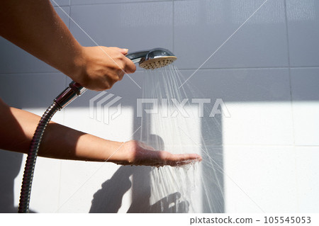 Female hand touching water pouring from a rain shower head, checking water temperature 105545053
