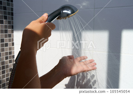 Female hand touching water pouring from a rain shower head, checking water temperature 105545054