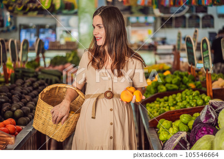 A glowing pregnant woman after forty makes a healthy choice as she selects organic vegetables and fruits at the vibrant organic market, prioritizing her well-being and her baby's health 105546664
