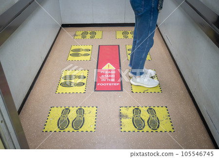 Woman standing on yellow footprint sign in lift or elevator and keep space for avoid spreading of virus disease in covid-19 pandemic. Woman standing on yellow footprint sign in lift or elevator and keep space for avoid spreading of virus disease in covid-19 pandemic. 105546745