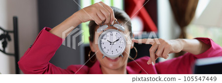 Woman in office points to alarm clock in her hand. 105547449