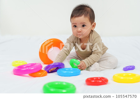 infant baby playing the pyramid toy with colored rings on bed 105547570