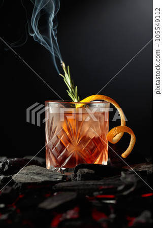 Old-fashioned cocktail with a burning twig of rosemary. Old-fashioned cocktail with a burning twig of rosemary. 105549112