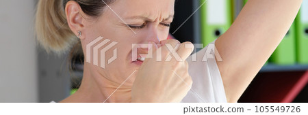 Worried woman with unhappy face checking smell of her armpit in office. Worried woman with unhappy face checking smell of her armpit in office. 105549726