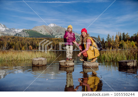 Mother with daughter standing on wooden steps on the shore of the lake in mountains. 105550244