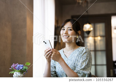 A woman operating a smartphone in a cafe looking at the camera A woman operating a smartphone in a cafe looking at the camera 105550267