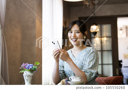 一位女士在咖啡館裡操作智能手機，看著相機 105550268