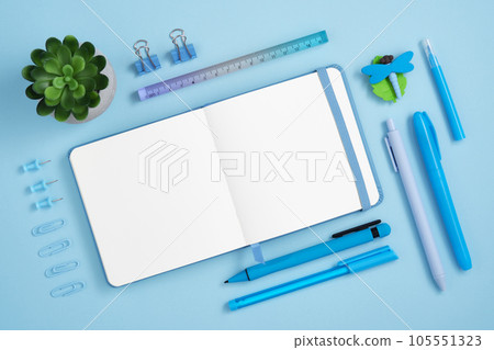 Blank notebook page with blue pen, pins, clips and dragonfly-shaped eraser on light blue background. Place for your text. 105551323