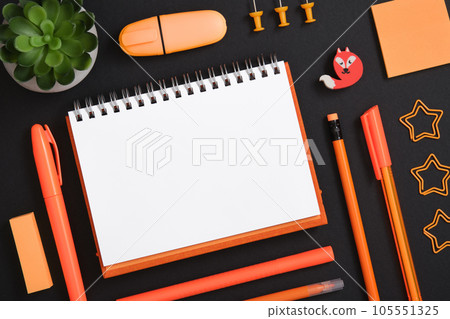 Blank notebook page for text in frame of orange school and office stationery set on black background. Eraser in the form of fox 105551325