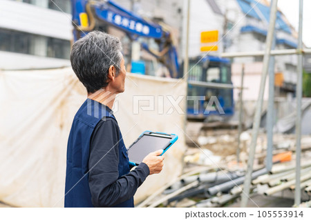 A craftsman holding a tablet and inspecting the construction site 105553914