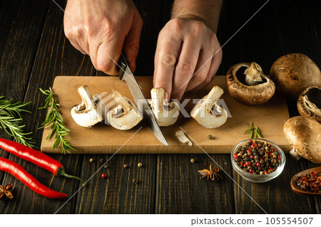 Slicing Agaricus mushrooms on a cutting board by the hands of a cook using a knife to prepare a delicious national dish. Peasant foods. 105554507