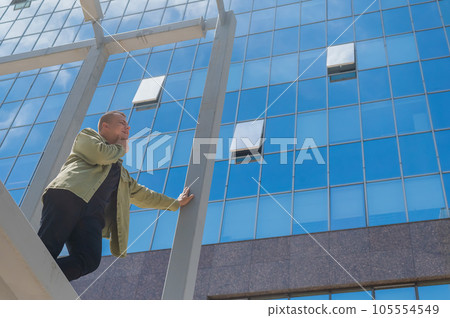 A pensive man stands against the backdrop of a skyscraper. 105554549