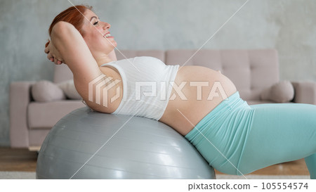 Pregnant red-haired woman doing fitball exercises at home. Pregnant red-haired woman doing fitball exercises at home. 105554574