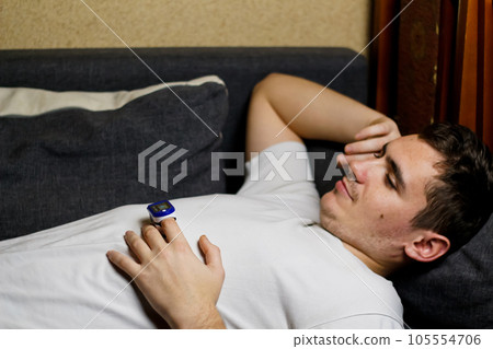 Caucasian man is ill on the sofa at home and he uses a pulse oximetry to check the saturation during the coronavirus epidemic. Selective focus Caucasian man is ill on the sofa at home and he uses a pulse oximetry to check the saturation during the coronavirus epidemic. Selective focus 105554706