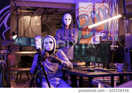 Criminals recording scam message on mobile phone camera and doing illegal online activities. Two anonymous hackers in hoods calling victim on smartphone videocall to steal privacy information 105556336