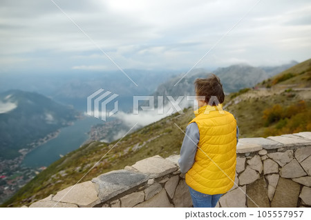 Tourist woman is admiring of aerial top view of mountains range and Boka Kotorska bay of Adriatic sea, Montenegro from outside observation deck. Lovcen national park. 105557957