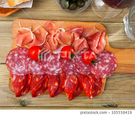 Spanish tapas - slicing sausages and jamon served on wooden board 105558419