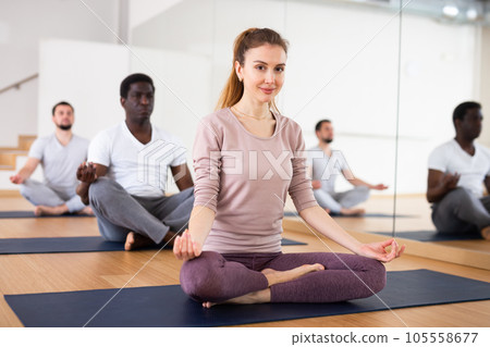 Woman sitting in lotus pose doing yoga meditation with group Woman sitting in lotus pose doing yoga meditation with group 105558677