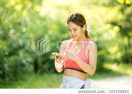 A beautiful woman wearing sportswear and exercising while listening to music on her smartphone in the park 105559263
