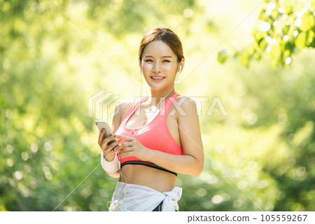 A beautiful woman wearing sportswear and exercising while listening to music on her smartphone in the park A beautiful woman wearing sportswear and exercising while listening to music on her smartphone in the park 105559267