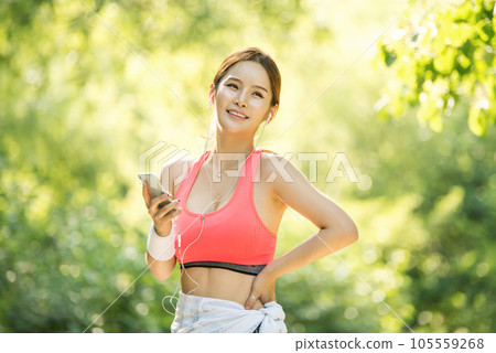 A beautiful woman wearing sportswear and exercising while listening to music on her smartphone in the park A beautiful woman wearing sportswear and exercising while listening to music on her smartphone in the park 105559268