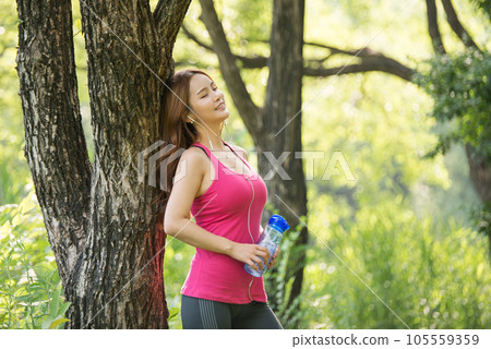A beautiful woman holding a water bottle in the park while listening to music during morning exercise A beautiful woman holding a water bottle in the park while listening to music during morning exercise 105559359