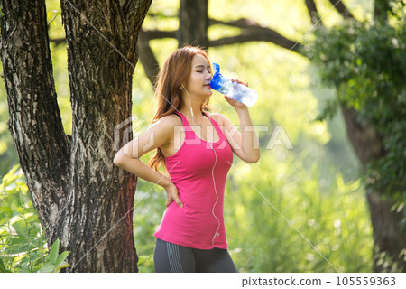 A beautiful woman holding a water bottle in the park while listening to music during morning exercise A beautiful woman holding a water bottle in the park while listening to music during morning exercise 105559363