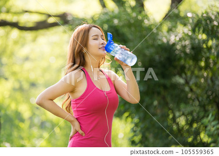 A beautiful woman holding a water bottle in the park while listening to music during morning exercise A beautiful woman holding a water bottle in the park while listening to music during morning exercise 105559365