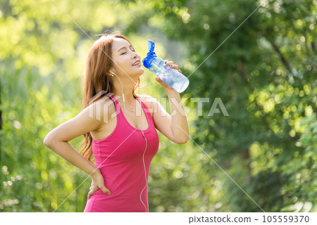 A beautiful woman holding a water bottle in the park while listening to music during morning exercise A beautiful woman holding a water bottle in the park while listening to music during morning exercise 105559370