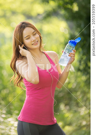 A beautiful woman holding a water bottle in the park while listening to music during morning exercise A beautiful woman holding a water bottle in the park while listening to music during morning exercise 105559399