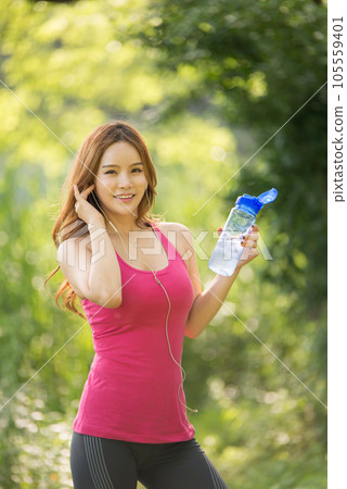 A beautiful woman holding a water bottle in the park while listening to music during morning exercise 105559401