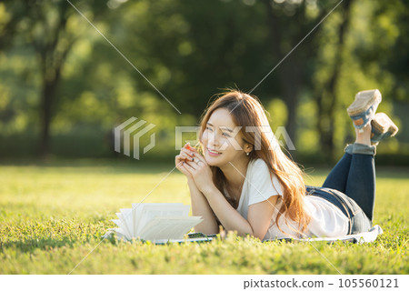 a beautiful woman lying on the park lawn reading 105560121
