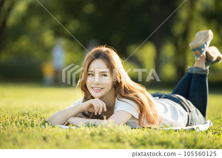 a beautiful woman lying on the park lawn reading 105560125