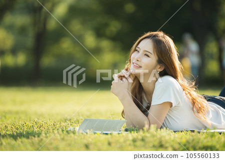 a beautiful woman lying on the park lawn reading 105560133
