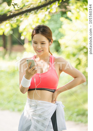 A beautiful woman wearing sportswear and exercising while listening to music on her smartphone in the park 105560344