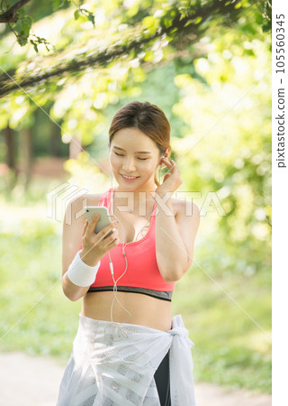 A beautiful woman wearing sportswear and exercising while listening to music on her smartphone in the park 105560345