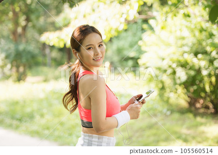 A beautiful woman wearing sportswear and exercising while listening to music on her smartphone in the park A beautiful woman wearing sportswear and exercising while listening to music on her smartphone in the park 105560514