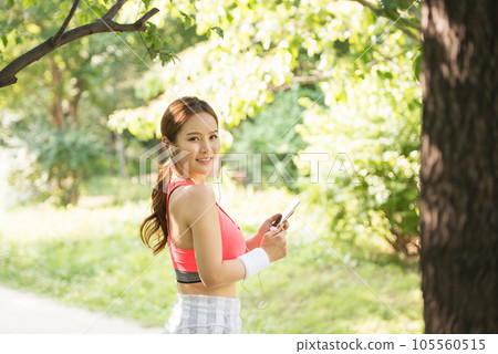 A beautiful woman wearing sportswear and exercising while listening to music on her smartphone in the park 105560515