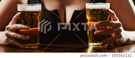 two glasses of light foam beer lager in the hands of a woman with big sexy breasts at the bar 105562132