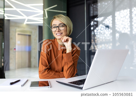Portrait of a young beautiful business woman at the workplace inside the office, the female worker is using a laptop smiling and looking contentedly at the camera. 105563081
