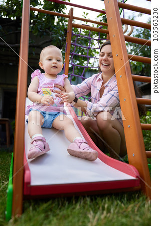 little baby girl with mother on slide in playground little baby girl with mother on slide in playground 105563230