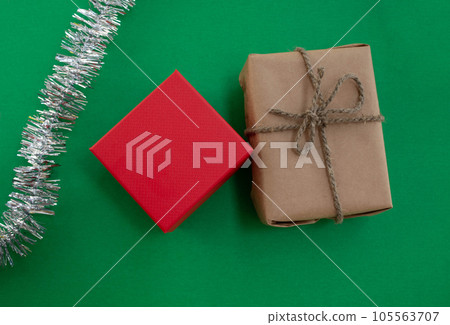 New Year gifts. A gift in craft paper, a gift in a red box and tinsel on a green background. New Year gifts. A gift in craft paper, a gift in a red box and tinsel on a green background. 105563707