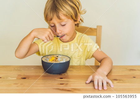 Happy boy sitting and eating a fresh smoothie bowl with mango, dragon fruit, granola and chia seeds 105563955