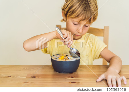 Happy boy sitting and eating a fresh smoothie bowl with mango, dragon fruit, granola and chia seeds 105563956
