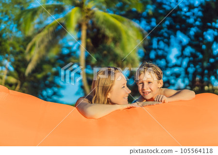 Summer lifestyle portrait of mother and son sitting on the orange inflatable sofa on the beach of tropical island. Relaxing and enjoying life on air bed Summer lifestyle portrait of mother and son sitting on the orange inflatable sofa on the beach of tropical island. Relaxing and enjoying life on air bed 105564118